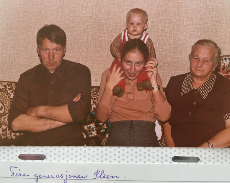 Familiebilde med fire personar i sofa. Ung kvinne i midten med baby på skuldrane, mann til venstre, eldre kvinne til høgre. Fotografert i 1980.