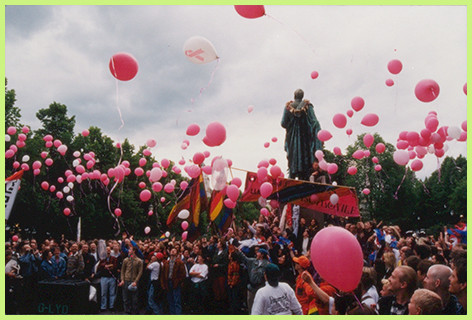 Queer parade, many people, several pink gas balloons in the air