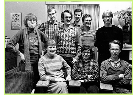 A black and white group photo of people, three of them sitting in the front, others standing behind them.